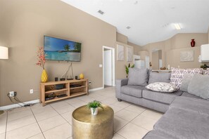 Ein modernes Wohnzimmer mit einem grauen Sofa, einer Holzunterhaltungsecke und einem runden Couchtisch mit einer Pflanze.
