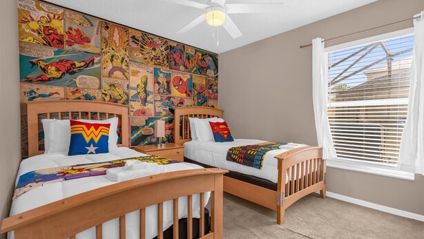 A bedroom with two wooden beds, a ceiling fan, a large comic book mural on the wall, and a window with blinds. - 5BR Family Fun Home | Game Room & Private Pool (Kissimmee)