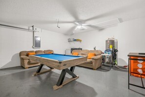Ein Zimmer mit Billardtisch, zwei Sofas, Deckenventilator und Warmwasserbereiter.