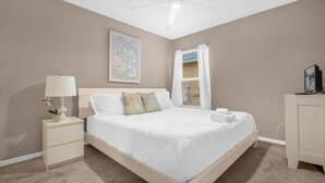 A bedroom with a bed, nightstand, lamp, and a painting on the wall. - 5BR Family Fun Home | Game Room & Private Pool (Kissimmee)