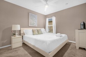 A bedroom with a bed, nightstand, lamp, and a painting on the wall. - 5BR Family Fun Home | Game Room & Private Pool (Kissimmee)