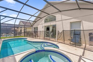 A swimming pool with a glass enclosure, a covered patio area, and a view of the surrounding neighborhood. - 5BR Family Fun Home | Game Room & Private Pool (Kissimmee)