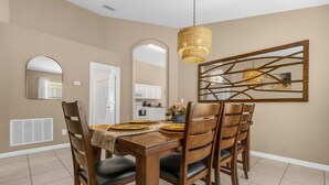 A dining room with a wooden table, six chairs, a woven pendant light, and a large mirror on the wall. - 5BR Family Fun Home | Game Room & Private Pool (Kissimmee)
