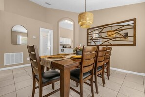 A dining room with a wooden table, six chairs, a woven pendant light, and a large mirror on the wall. - 5BR Family Fun Home | Game Room & Private Pool (Kissimmee)
