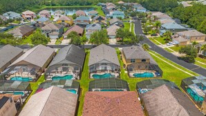 A residential area with houses, a swimming pool, and a lake in the background. - 5BR Family Fun Home | Game Room & Private Pool (Kissimmee)
