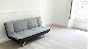 A grey sofa with a black frame and metal legs in a room with a white radiator and a window. - Torquay, 1 Bedroom, Sleeps 4, Free Parking, Torbay (Torquay)