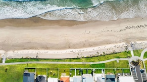 Vista aérea de una zona costera con playa, un sendero cubierto de hierba y edificios con diversas estructuras.