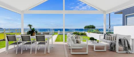Une vaste terrasse extérieure offrant une vue sur l’océan, aménagée avec des chaises blanches et un canapé.