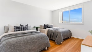 A bedroom with two beds, a large window, and a plant. - La Palma Beach House ~ Charming coastal retreat (Warilla)
