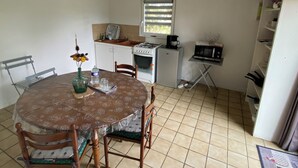 Uma cozinha compacta com mesa, cadeiras, fogão, geladeira e micro-ondas.
