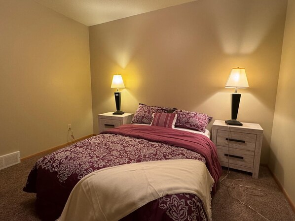 Une chambre à coucher avec un lit, deux tables de chevet avec des lampes, un sol recouvert d’une moquette et une prise électrique au mur.