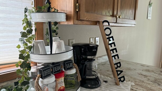 Un comptoir de cuisine aménagé en coin café, comprenant une machine à café, du sucre, de la crème et des tasses à café.