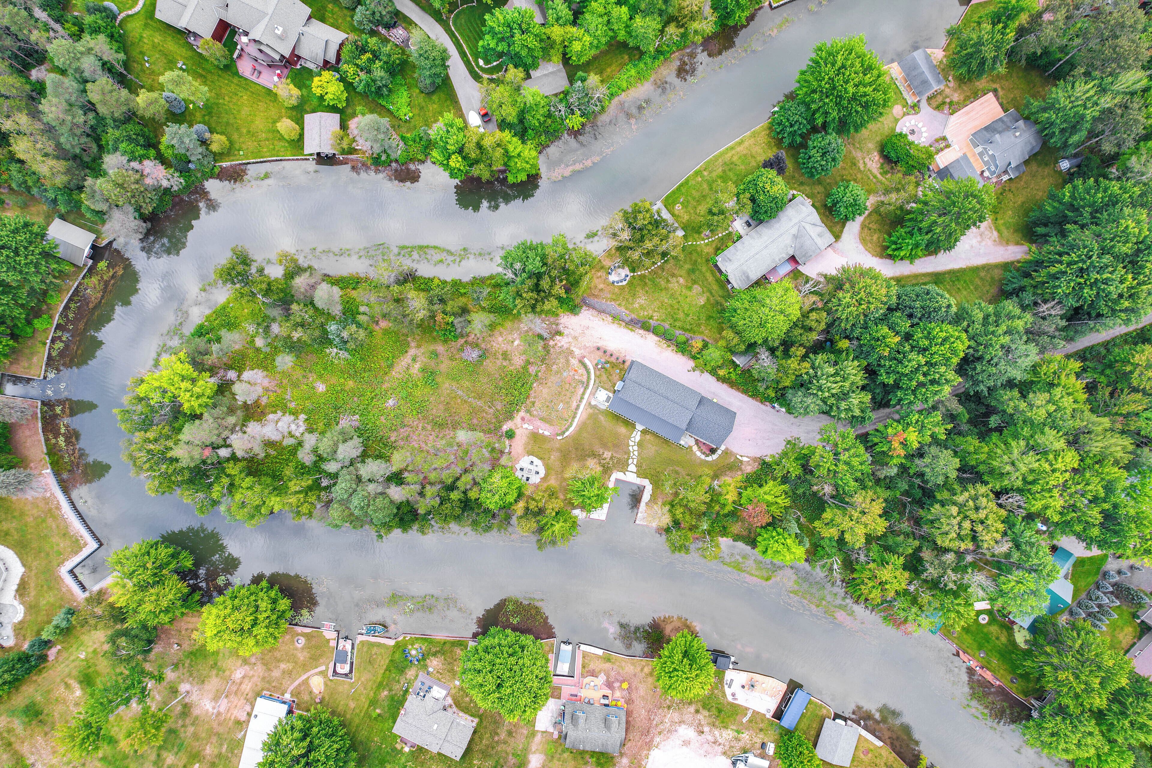An aerial view of a residential area with houses, a river, and surrounding greenery.
