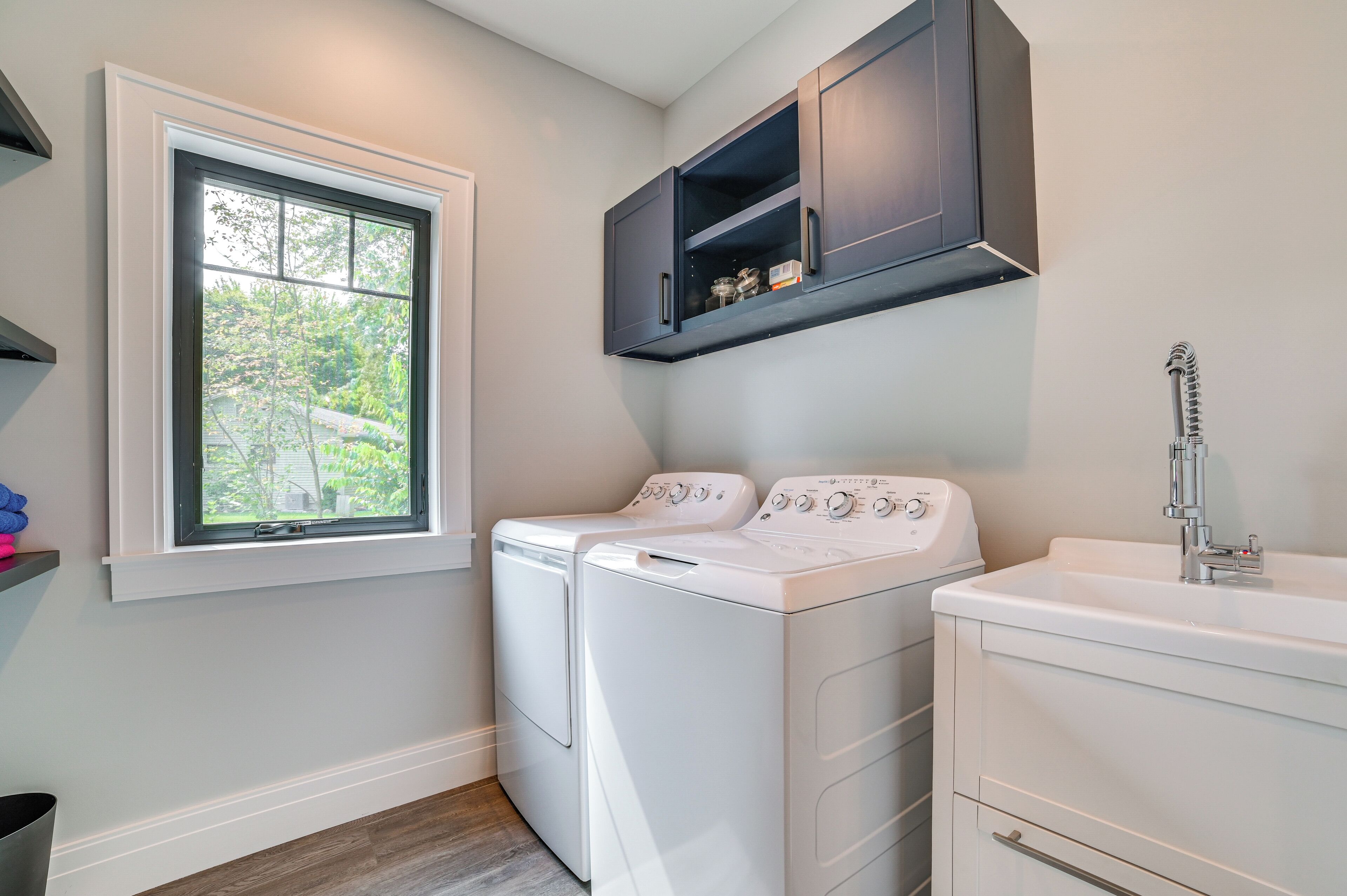 A laundry room with two white front-loading washers and a white sink with a chrome faucet.