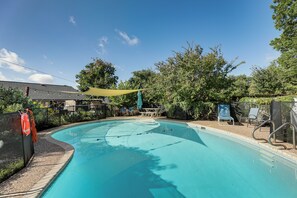 A swimming pool with a curved edge, surrounded by trees and a covered seating area.