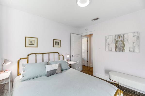 A bedroom with a bed, bedside table, lamp, and a door leading to another room.