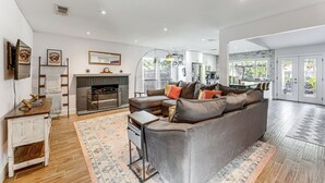 Ein modernes Wohnzimmer mit Ecksofa, Kamin und Essbereich, im Hintergrund eine Küche.