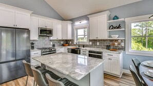 A modern kitchen with white cabinets, stainless steel appliances, a marble island, and a window with a view of greenery. - Hot Tub + Game Room! Family Connelly Springs Home (Connellys Springs)