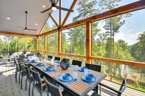 A covered outdoor dining area with a table set for six, surrounded by chairs, and overlooking a forested area with a body of water. - Hot Tub + Game Room! Family Connelly Springs Home (Connellys Springs)