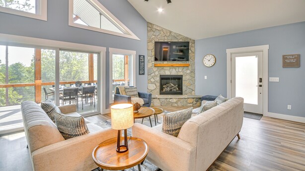 A spacious living room with a stone fireplace, large windows, and a ceiling fan. - Hot Tub + Game Room! Family Connelly Springs Home (Connellys Springs)