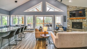 A spacious living area with a stone fireplace, a large TV mounted on the wall, and a dining area with a long table and chairs. - Hot Tub + Game Room! Family Connelly Springs Home (Connellys Springs)