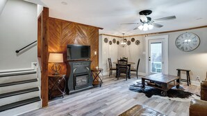 A living room with a fireplace, a television, a dining table with chairs, a clock on the wall, and a ceiling fan. - Pet-friendly Granbury Home w/ Yard, Near Downtown! (Granbury)