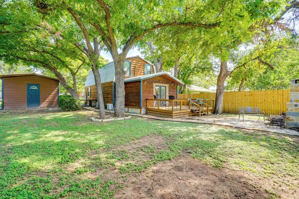 A wooden cabin with a deck, surrounded by trees and a fenced yard. - Pet-friendly Granbury Home w/ Yard, Near Downtown! (Granbury)