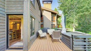 Um deck de madeira com mobiliário para área externa, um espaço de estar coberto e vista para o interior da casa.