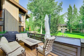 An outdoor deck with a wooden table, two sofas, and a grill.