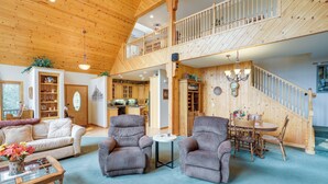 A spacious living room with a high ceiling, wooden staircase, and a dining area with a table and chairs. - Cozy Chester Home w/ Patio & Lake Access! (Chester)
