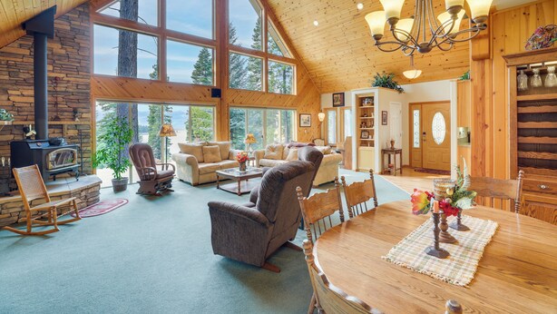 A spacious living area with a large wooden ceiling, a stone fireplace, and a dining table set with a placemat and flowers. - Cozy Chester Home w/ Patio & Lake Access! (Chester)