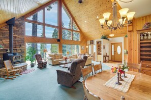 A spacious living area with a large wooden ceiling, a stone fireplace, and a dining table set with a placemat and flowers. - Cozy Chester Home w/ Patio & Lake Access! (Chester)