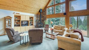 A cozy living room with wooden ceilings, a stone fireplace, and large windows offering a forest view. - Cozy Chester Home w/ Patio & Lake Access! (Chester)
