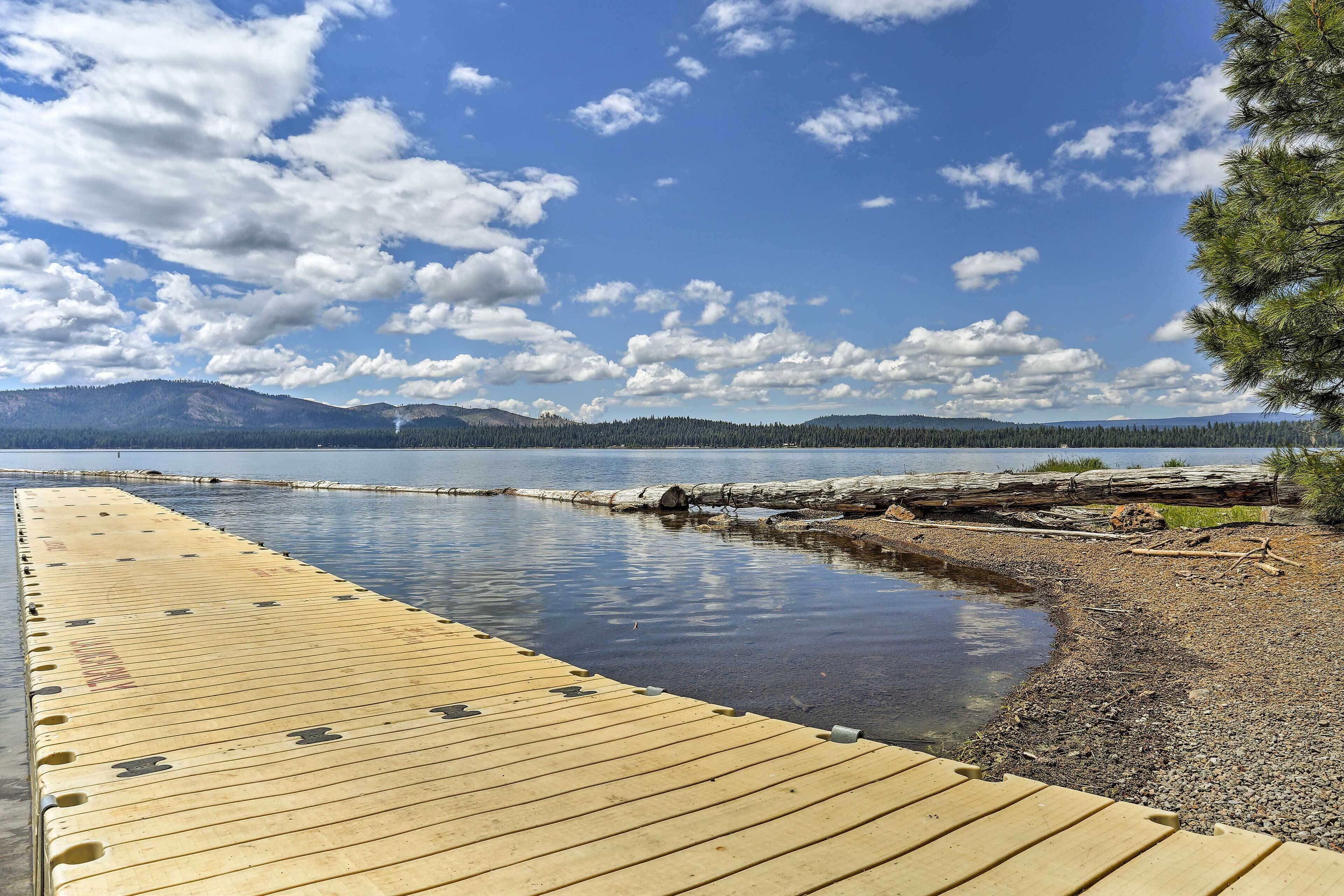 Une jetée en bois s’étendant sur un lac paisible, avec une chaîne de montagnes boisées en arrière-plan.