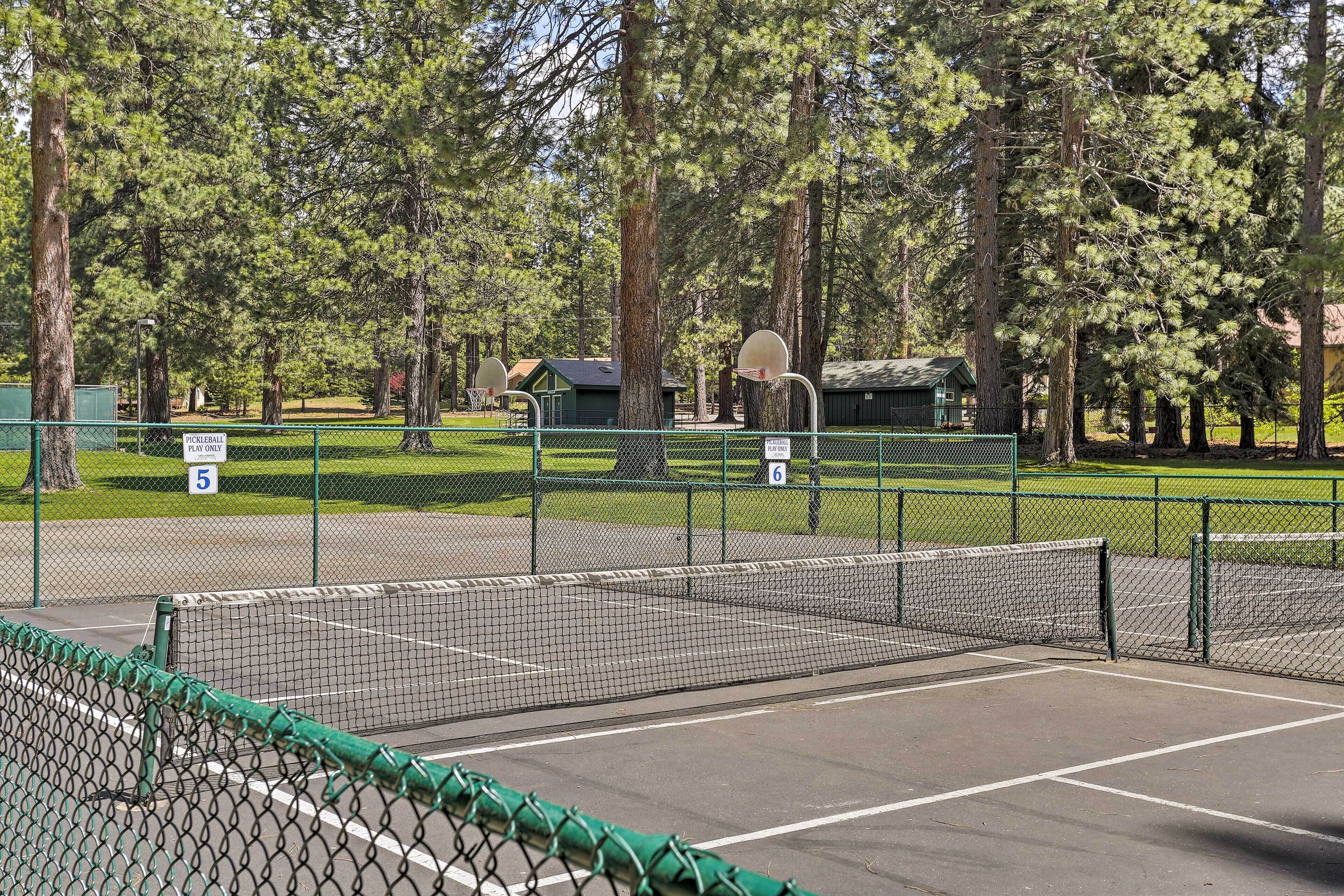 A tennis court with a net, surrounded by trees and a small building in the background.