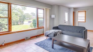 A living room with a grey sofa, a coffee table, and a large window with curtains. - Pet-friendly New Berlin Retreat w/ Patio & Yard! (New Berlin)