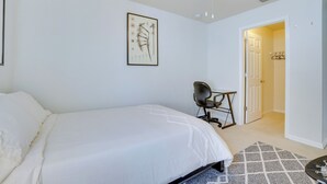 A bedroom with a bed, a chair, a ceiling fan, a door, and a wall-mounted artwork.