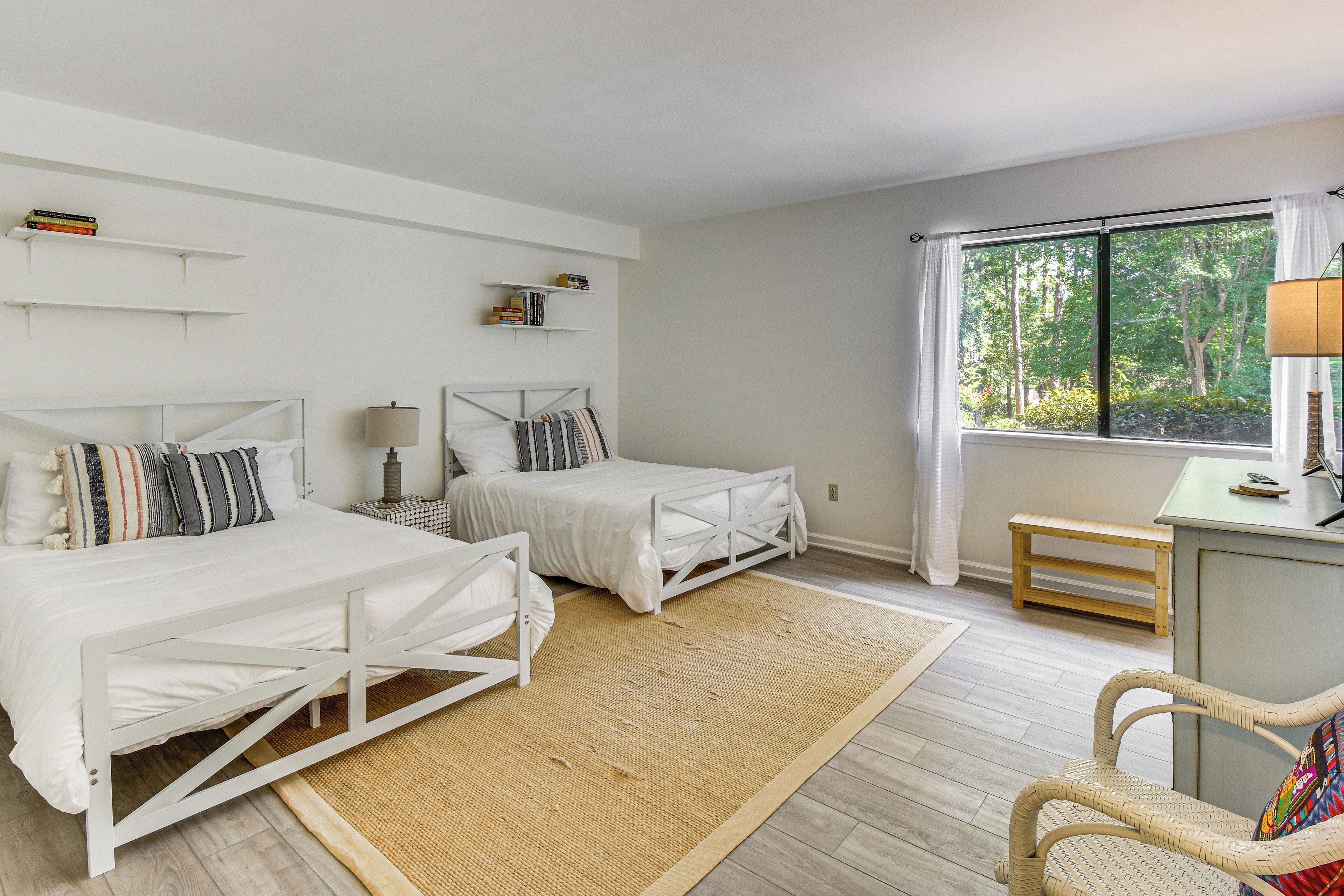 A bedroom with two beds, a desk, and a window with a view of trees.