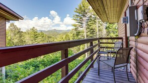 A wooden deck with a railing, a table, and two chairs, overlooking a forested area with mountains in the distance. - Bryson City Cabin in Smoky Mtn w/ Resort Amenities (Bryson City)