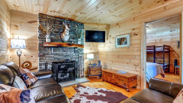A log cabin interior with a stone fireplace, leather sofas, a television, and a wooden bunk bed. - Bryson City Cabin in Smoky Mtn w/ Resort Amenities (Bryson City)