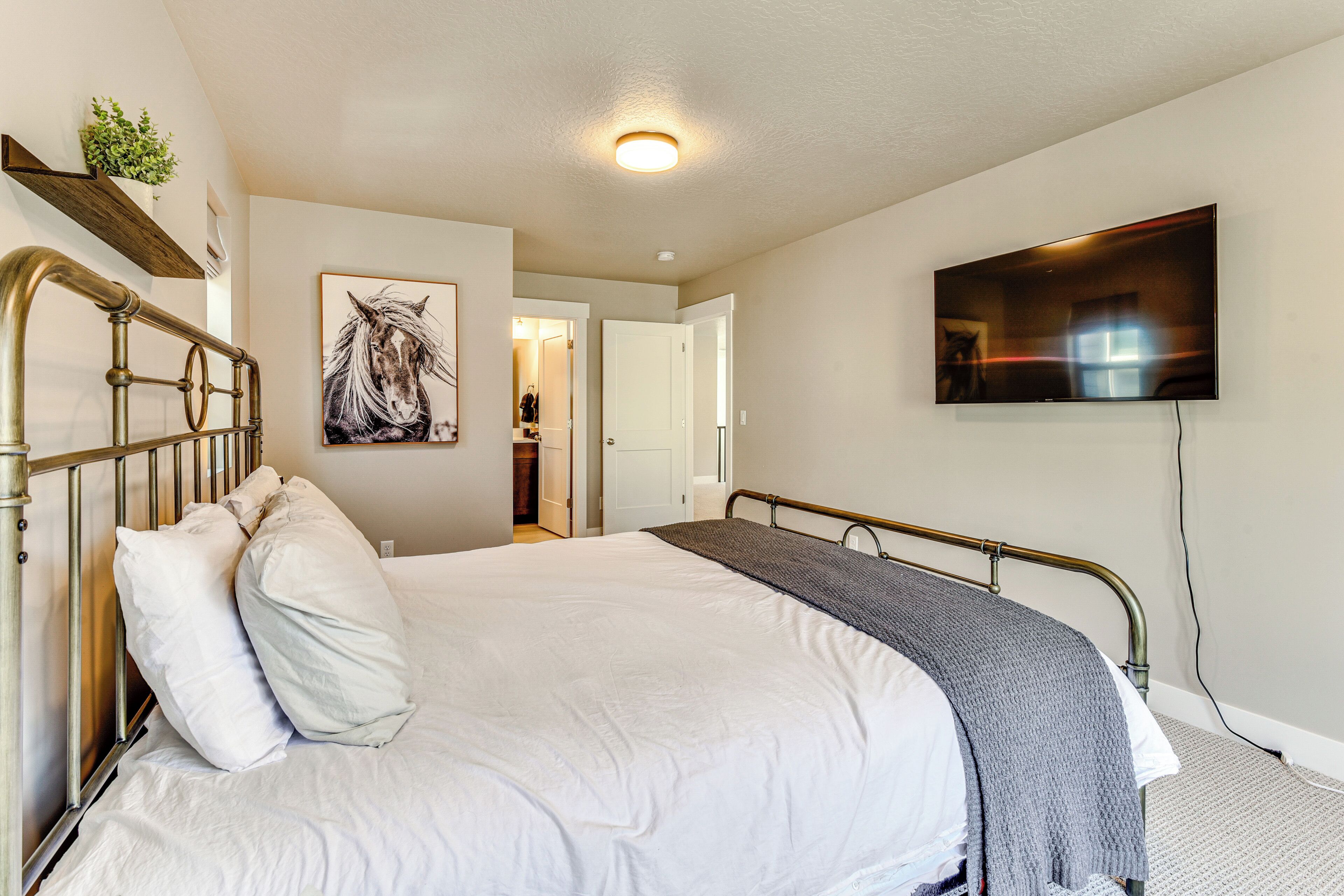 A bedroom with a large bed, a mounted TV, and a door leading to another room.