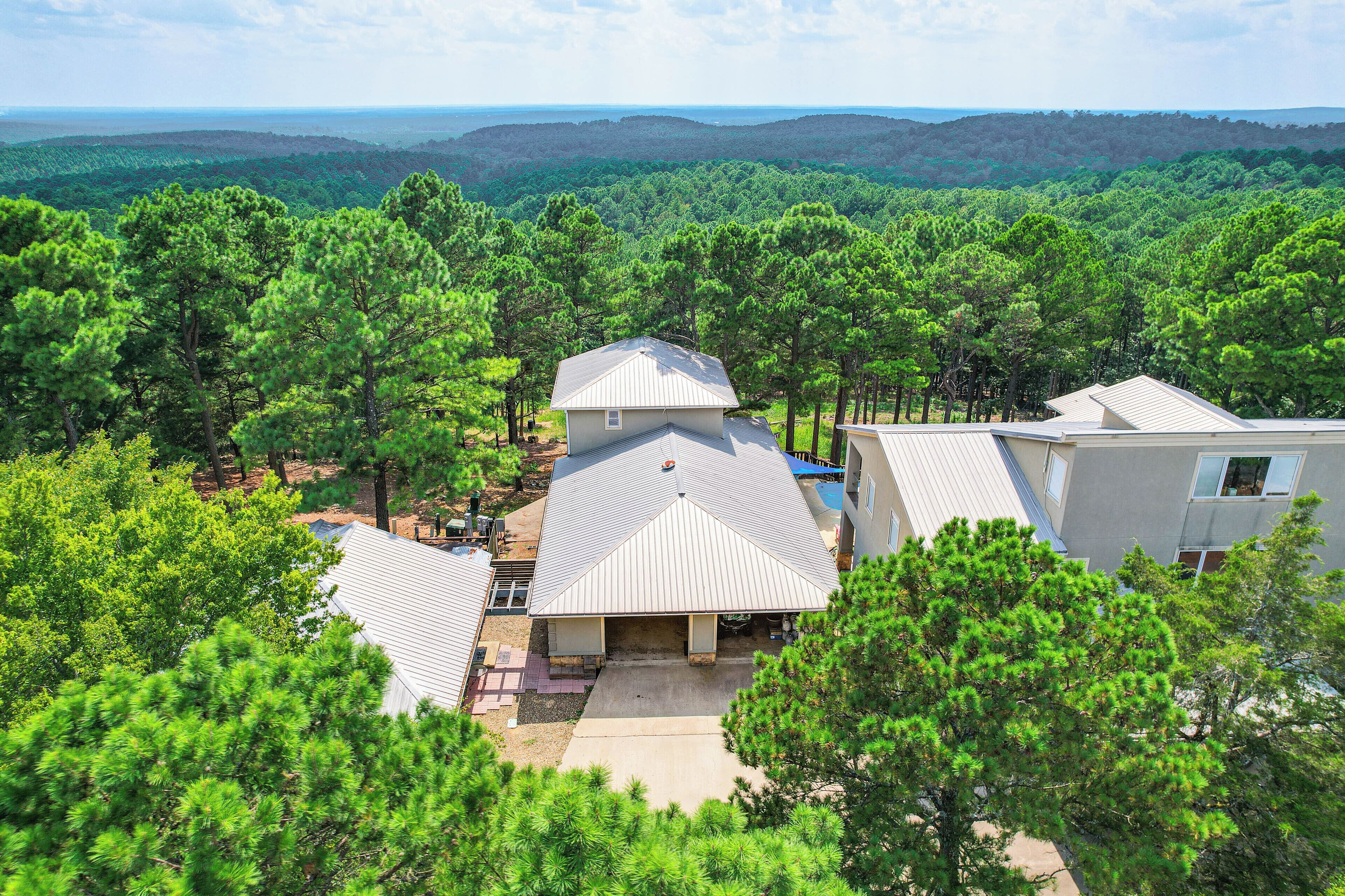 A residential area with multiple houses surrounded by dense pine forests and a distant view of hills.