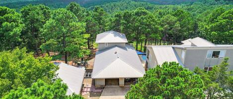 A residential area with multiple houses surrounded by dense pine forests and a distant view of hills.