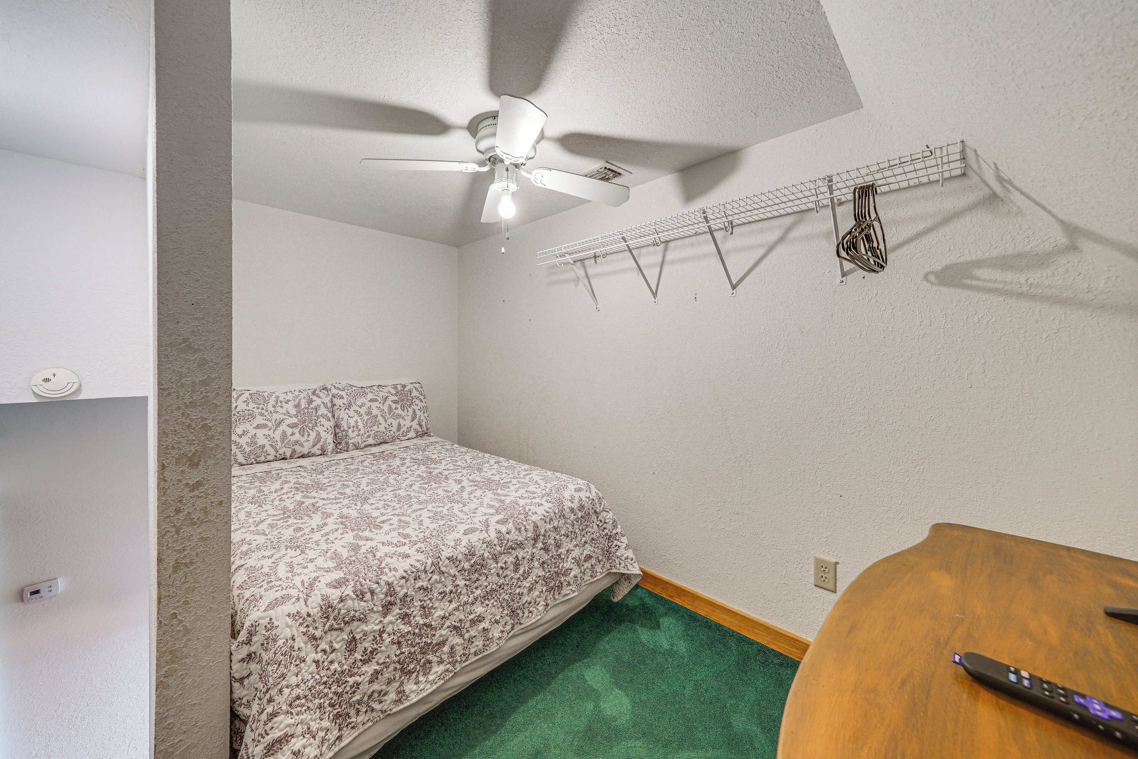 A bedroom with a bed, a ceiling fan, a clothes rack, and a wooden table.