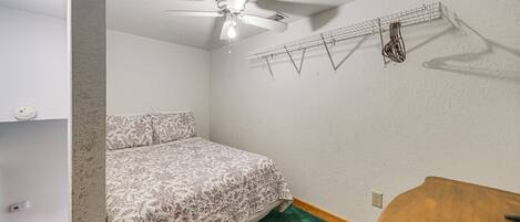 A bedroom with a bed, a ceiling fan, a clothes rack, and a wooden table.
