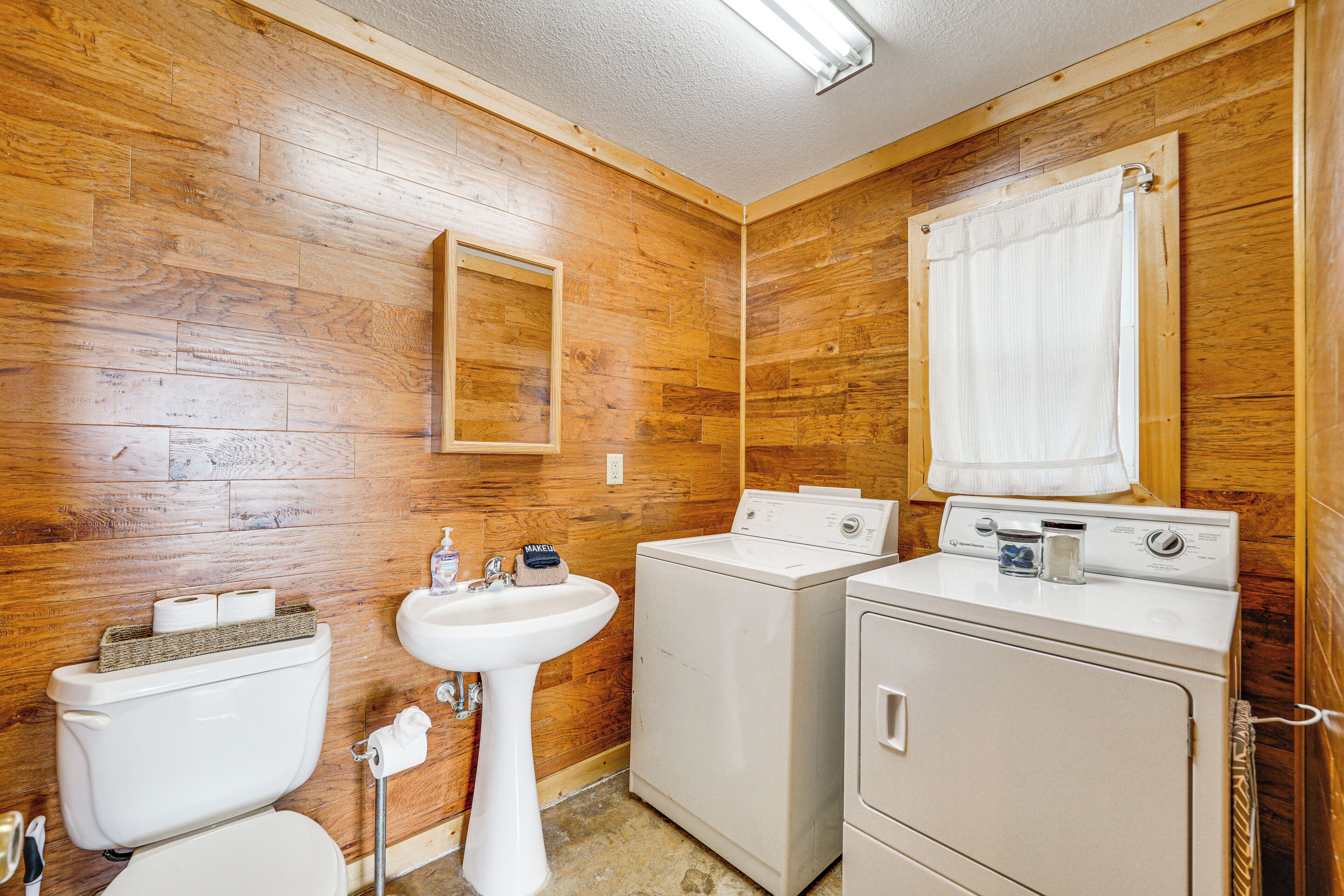 A bathroom with wooden walls, a sink, a toilet, and a washing machine.