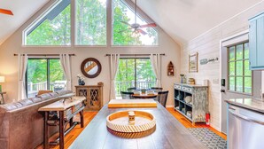 A spacious loft with high ceilings, large windows, a wooden dining table, a sofa, and a kitchen area. - Lakefront Murphy Getaway w/ Deck, Dock & Kayaks! (Murphy)