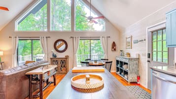 A spacious loft with high ceilings, large windows, a wooden dining table, a sofa, and a kitchen area.