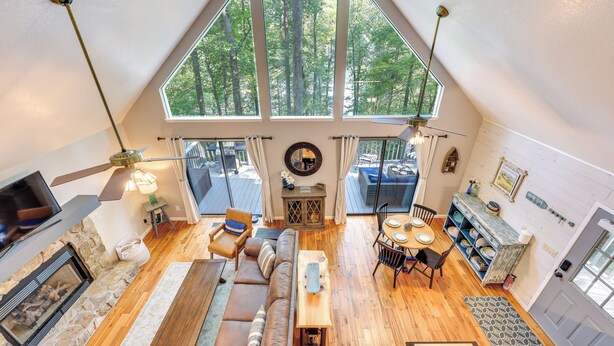 A spacious loft with a high ceiling, a stone fireplace, a wooden dining table, a sofa, and a large window offering a view of trees. - Lakefront Murphy Getaway w/ Deck, Dock & Kayaks! (Murphy)