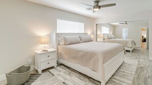 A bedroom with a large bed, bedside tables, a mirror, and a ceiling fan.